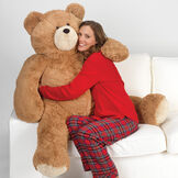 4' Big Hunka Love Bear - Seated golden brown bear with a female model in red pajamas on a sofa image number 0