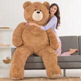 6' Giant Hunka Love Bear - Seated golden brown bear with a model in lavender pajamas on a sofa image number 3