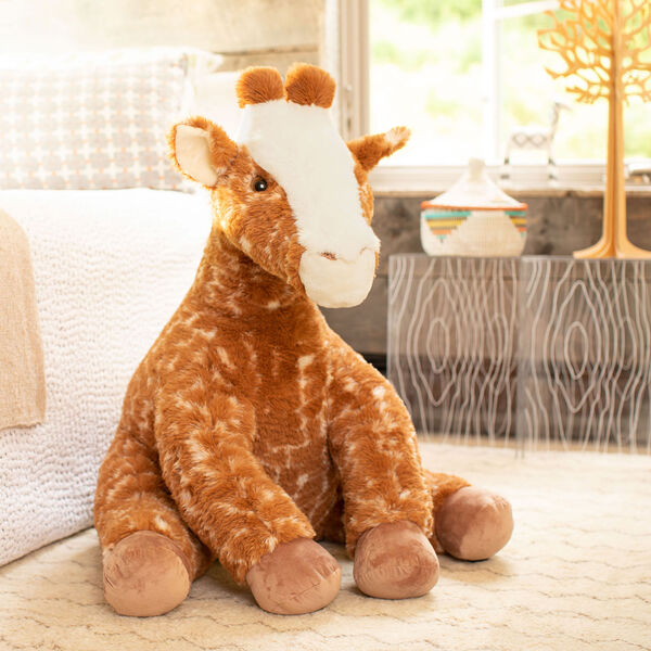 3 1/2' Gentle Giant Giraffe - Three quarter view of seated soft giraffe in bedroom scene