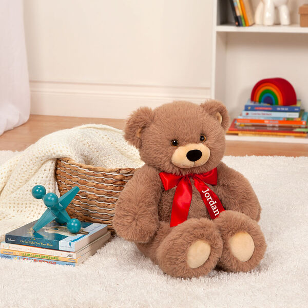 18" Oh So Soft Teddy Bear - Front view of seated honey brown bear with red satin bow in a living room scene
