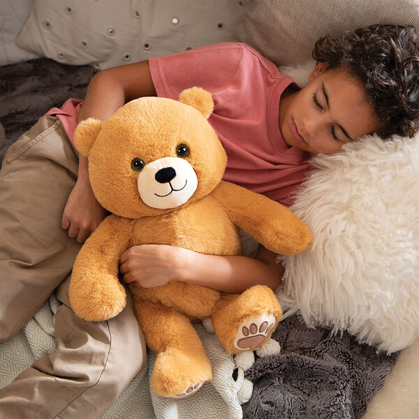 20" Hugsy the Teddy Bear - Front view of seated golden brown bear with model in a bedroom scene