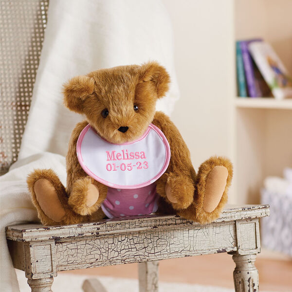 15" Baby Girl Bear - Jointed honey bear dressed in pink with white dots fabric diaper and bib sitting on a table with a bookcase behind it.  image number 1