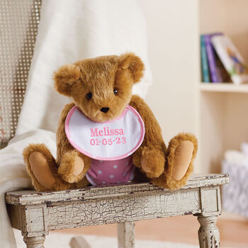 15" Baby Girl Bear - Jointed honey bear dressed in pink with white dots fabric diaper and bib sitting on a table with a bookcase behind it. 