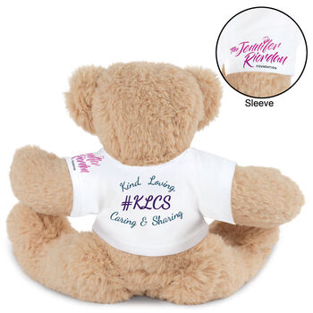 15" Spark Kindness Bear - Back view of seated soft caramel brown bear dressed in a white t-shirt with blue and purple graphics that says "#KLCS" surrounded by "Kind, Loving, Caring, and Sharing" 